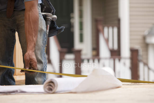 Carpinteiro hispânico tomando uma medida de seus planos no canteiro de obras de construção — Fotografia de Stock