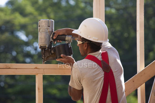 Carpinteiro hispânico usando uma pistola de prego em uma moldura da janela — Fotografia de Stock