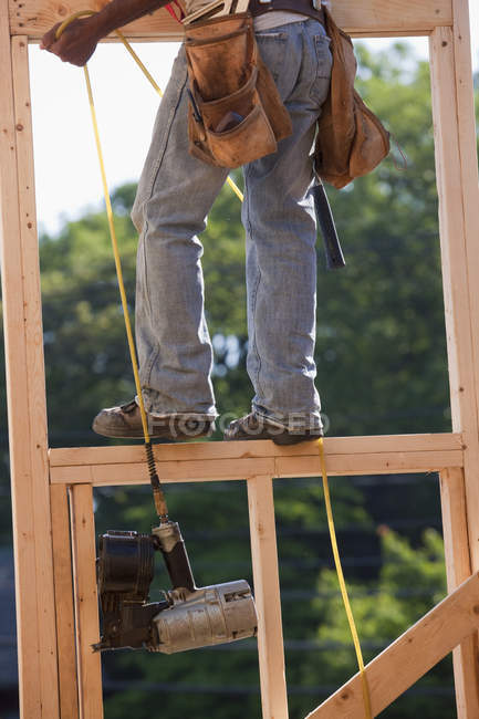 Carpinteiro puxando pistola de prego até o segundo andar de uma casa em construção — Fotografia de Stock