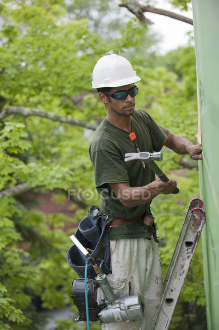 Hispanic carpenter hammering exterior sheathing on the upper floor of a house — Stock Photo