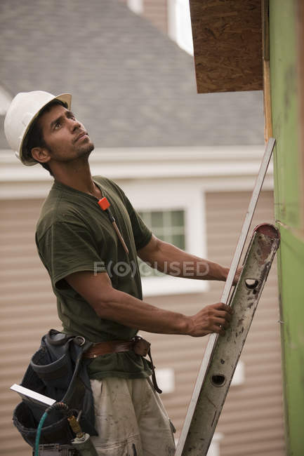 Carpinteiro hispânico em uma escada com um nível em uma casa em construção — Fotografia de Stock