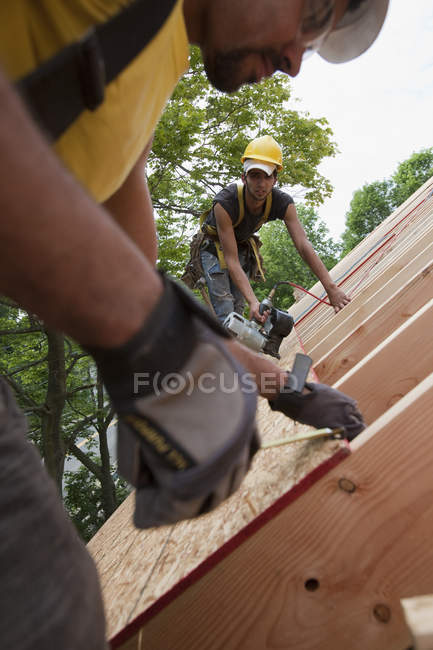 Charpentiers hispaniques mesurant et clouant panneau de toit à une maison en construction — Photo de stock