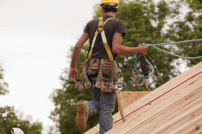 Carpinteiro hispânico andando no telhado de uma casa em construção — Fotografia de Stock