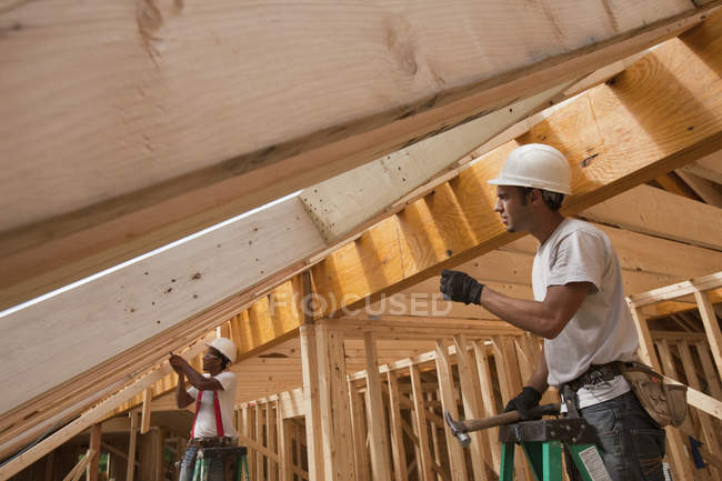 Carpinteiros hispânicos trabalhando em vigas de telhado em uma casa em construção — Fotografia de Stock