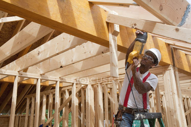 Carpinteros hispanos usando sierra alternativa en una viga de techo en una casa en construcción - foto de stock