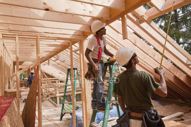 Carpinteros hispanos usando cinta métrica en una casa en construcción - foto de stock