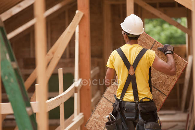 Carpinteiro hispânico segurando um painel de telhado em uma casa em construção — Fotografia de Stock