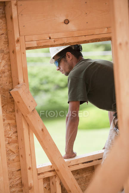 Carpinteiro hispânico olhando para fora da abertura da janela do segundo andar em uma casa em construção — Fotografia de Stock