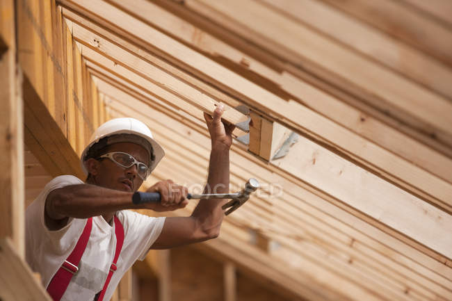 Carpinteiro hispânico martelando vigas de telhado em uma casa em construção — Fotografia de Stock