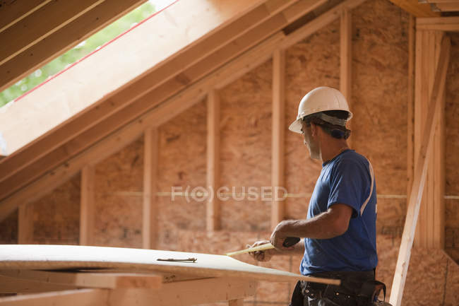 Carpinteiro hispânico medindo um pedaço de bainha em uma casa em construção — Fotografia de Stock