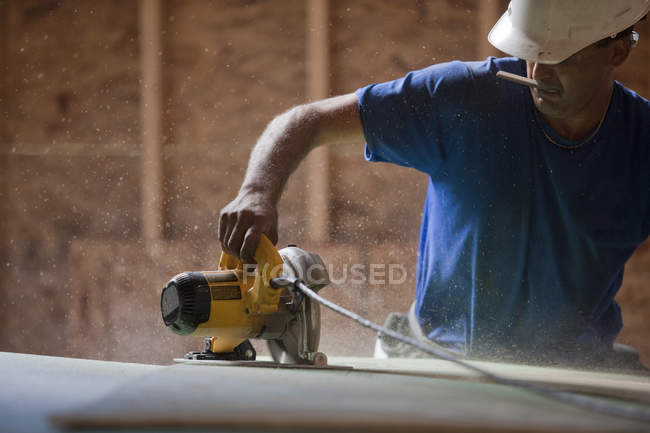 Hispanic carpenter using a circular saw on the roofing sheathing at a house under construction — Stock Photo