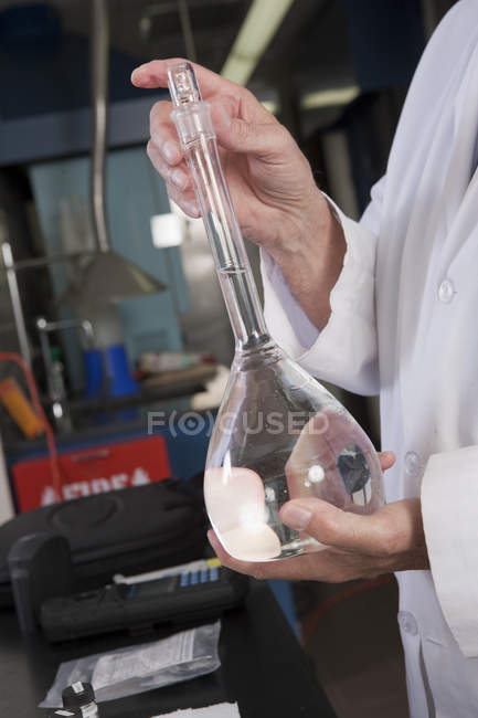 Immagine ritagliata dello scienziato che mescola il contenuto liquido del pallone nel laboratorio dell'impianto di trattamento delle acque — Foto stock