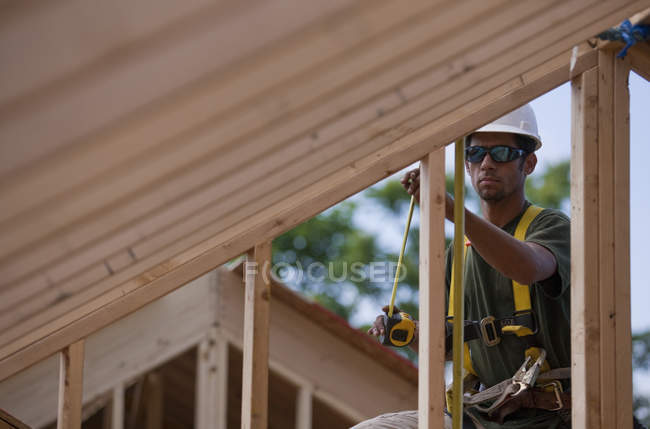 Hispanischer Tischler misst Wandbolzen an einem im Bau befindlichen Haus — Stockfoto