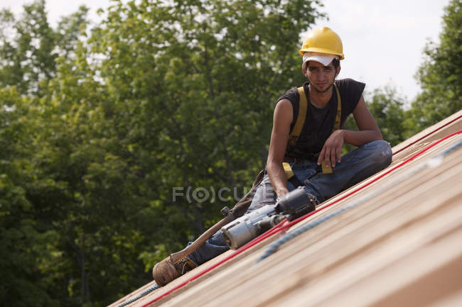 Charpentier hispanique reposant sur la construction du toit d'une maison avec un pistolet à clous — Photo de stock