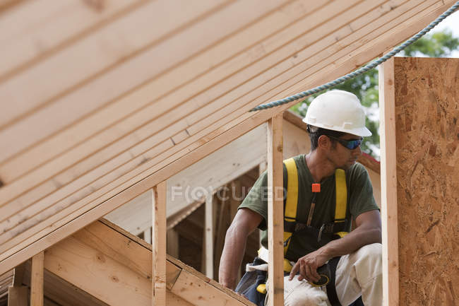 Carpintero hispano sosteniendo una cinta métrica en el piso superior de una casa en construcción - foto de stock