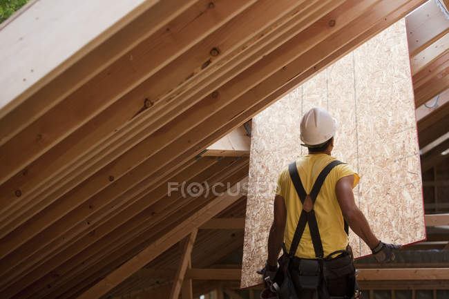 Hispanic carpenter pushing sheathing up to roof at a house under construction — Stock Photo