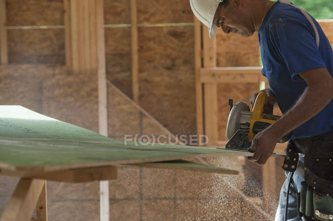 Carpenter cutting exterior sheathing with circular saw at a house under construction — Stock Photo