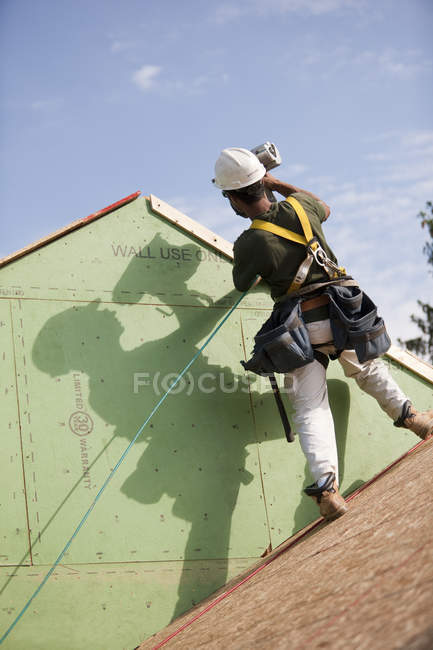 Carpinteiro hispânico usando uma pistola de pregos na guarnição do telhado de uma casa em construção — Fotografia de Stock