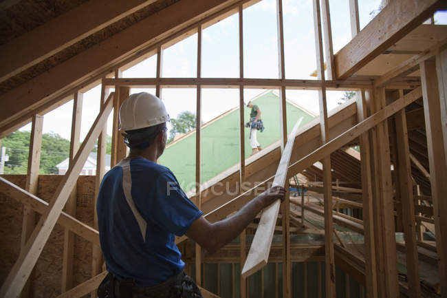Falegnami ispanici portando striscia assetto costruzione fino al tetto di una casa in costruzione — Foto stock
