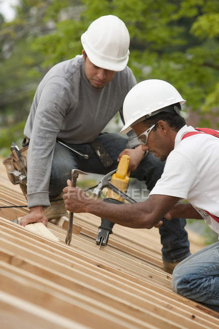 Menuisiers utilisant un sawzall et une barre d'accès sur le toit d'une maison en construction — Photo de stock