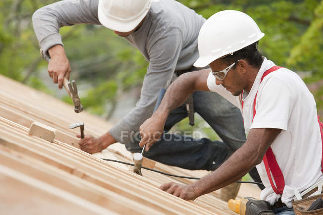 Falegnami ispanici che utilizzano martelli sul tetto di una casa in costruzione — Foto stock
