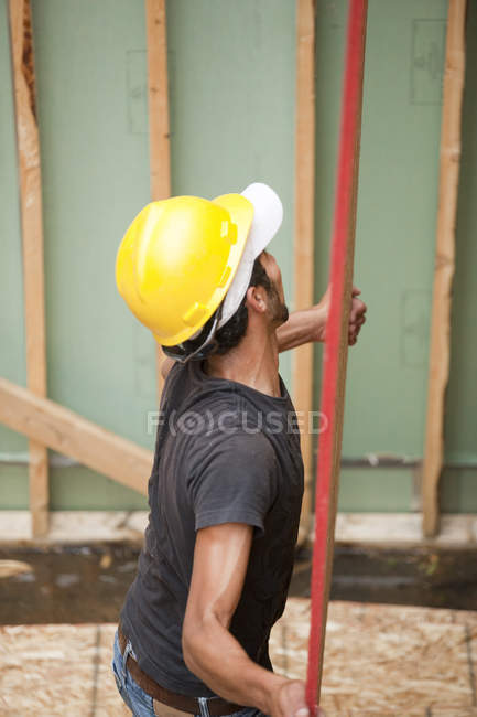 Hispanic carpenter lifting sheathing at a house under construction — Stock Photo