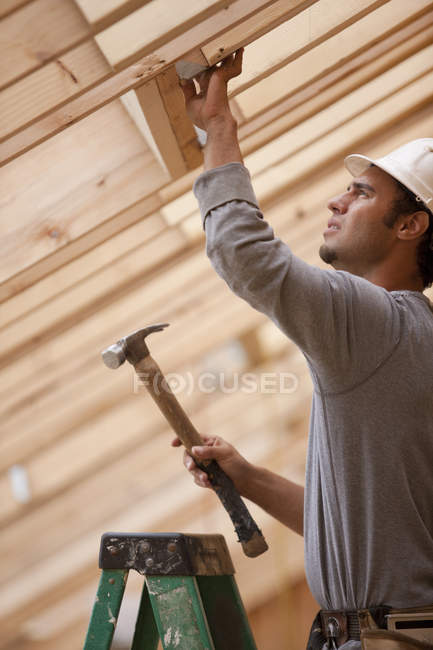 Hispanic carpenter hammering metal reinforcement bracing at a house under construction — Stock Photo