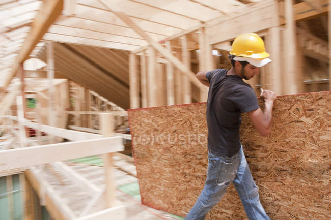 Hispanic carpenter carrying sheathing at a house under construction — Stock Photo