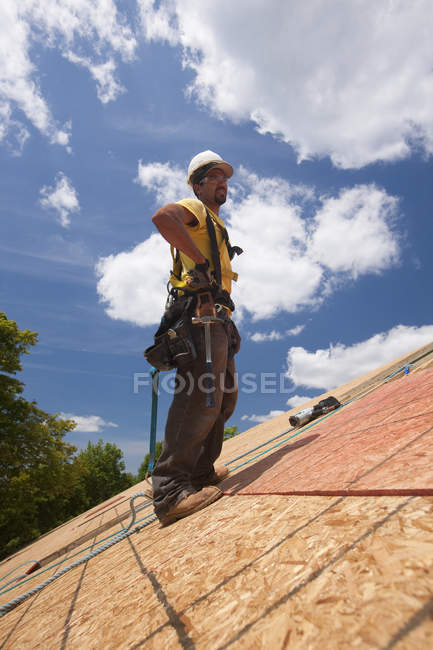 Carpintero hispano de pie sobre el techo de una casa en construcción - foto de stock