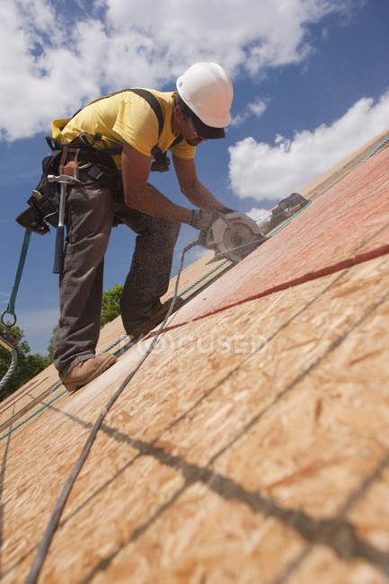 Carpenter using a circular saw on the roof panel at a house under construction site — Stock Photo