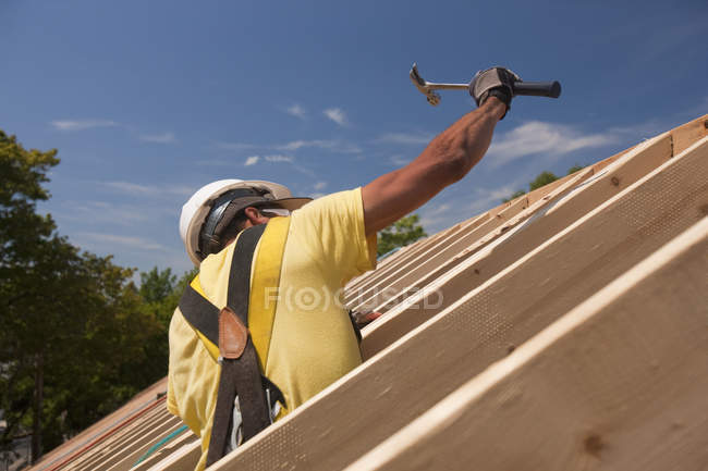 Falegname ispanico con un martello sul tetto di una casa in costruzione — Foto stock