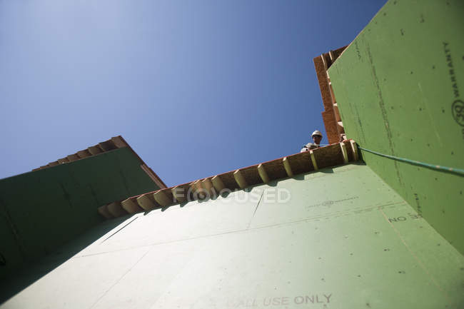 Carpinteiro hispânico pendurado sobre a borda do telhado em uma casa em construção — Fotografia de Stock