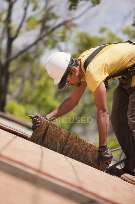 Carpintero hispano tirando del revestimiento de una casa en construcción - foto de stock