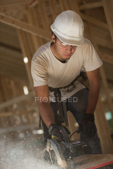 Carpintero usando una sierra circular en el panel del techo en una casa en construcción - foto de stock