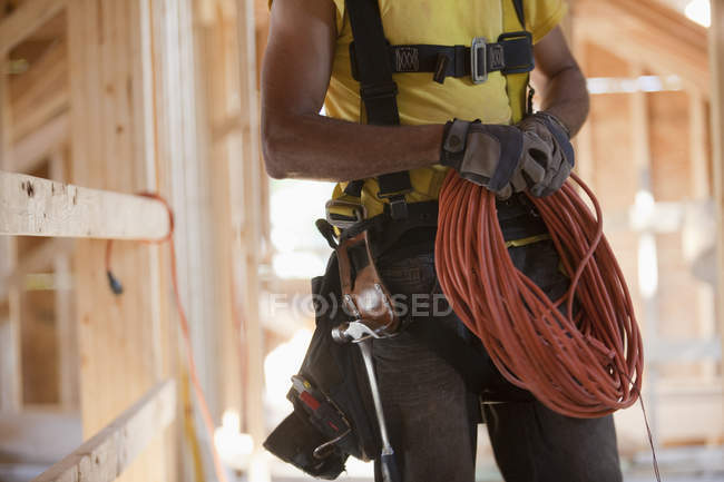 Carpinteiro hispânico enrolando cabo de alimentação elétrica em um canteiro de obras — Fotografia de Stock