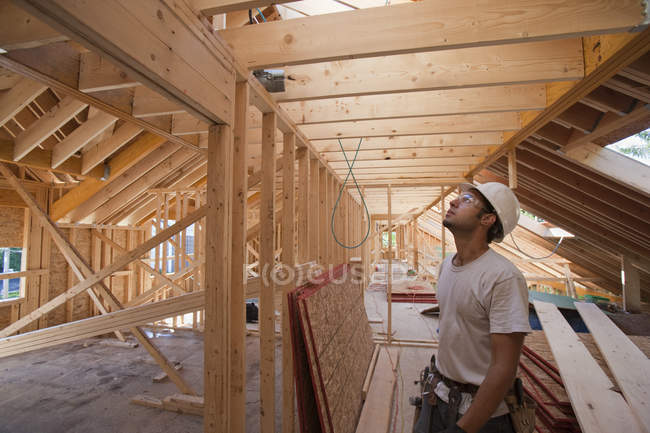 Charpentier hispanique regardant le toit à l'étage supérieur d'une maison en construction — Photo de stock