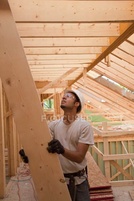 Carpinteiro hispânico passando uma viga para o telhado em uma casa em construção — Fotografia de Stock