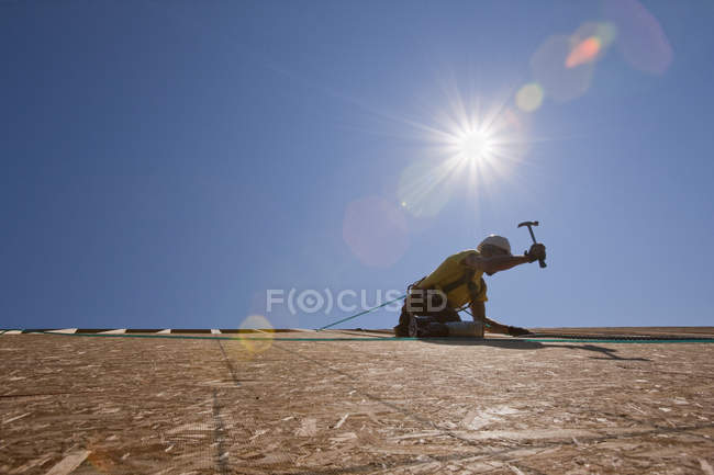 Charpentier hispanique utilisant un marteau sur la toiture d'une maison en construction — Photo de stock