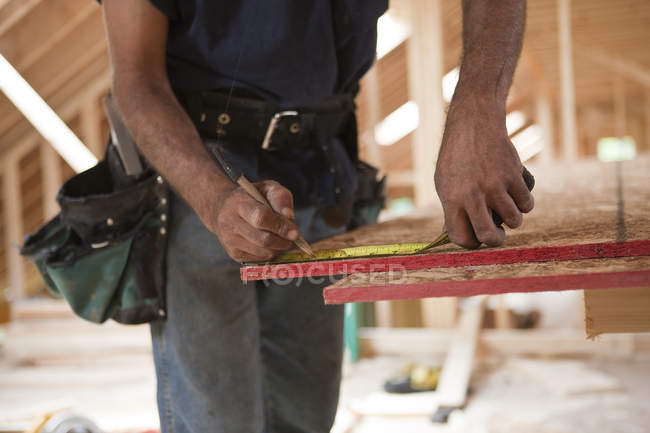 Carpinteiro hispânico medindo um painel de telhado de uma casa em construção — Fotografia de Stock