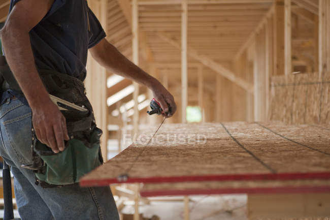 Falegname ispanico che spezza una corda su un pannello del tetto di una casa in costruzione — Foto stock