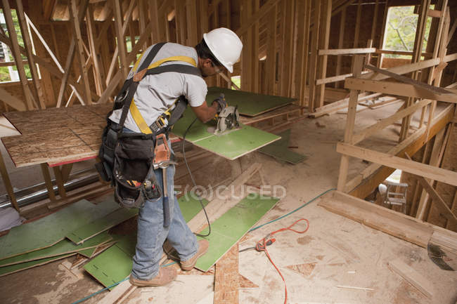 Carpinteiro usando uma serra circular na parede exterior embainhando em uma casa em construção — Fotografia de Stock