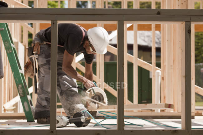 Charpentier sciant une planche sur un chantier de construction — Photo de stock