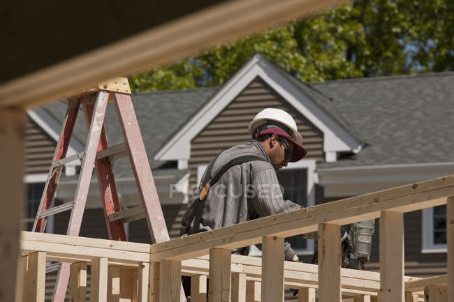 Carpinteiro usando pistola de prego no enquadramento em um canteiro de obras de construção — Fotografia de Stock