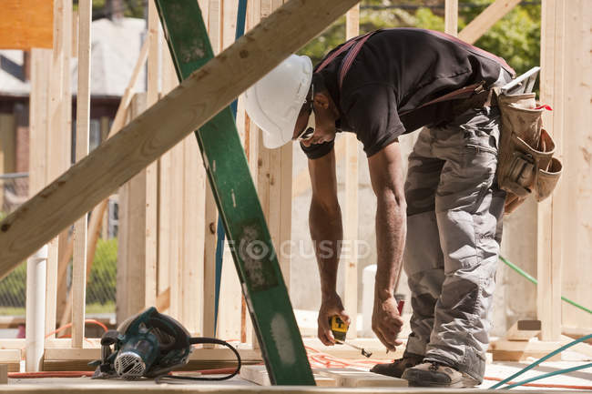 Medición del carpintero con cinta métrica en una obra de construcción - foto de stock