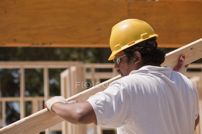 Carpenter carrying a wall stud at a building construction site — Stock Photo