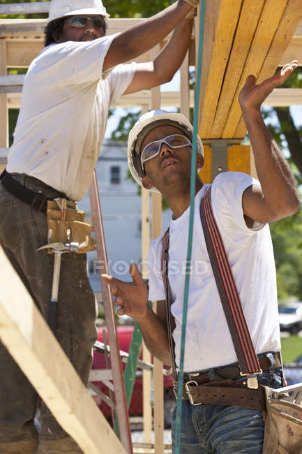 Carpinteros levantando vigas en una obra de construcción - foto de stock