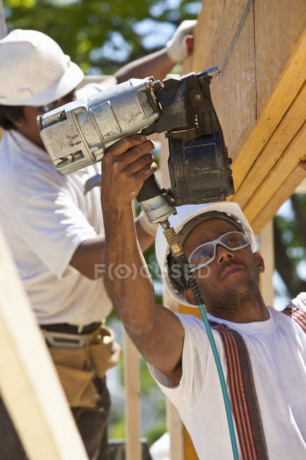 Carpinteros clavando vigas en un sitio de construcción de edificios - foto de stock