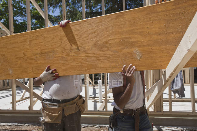 Carpinteiros levantando um feixe laminado em um canteiro de obras — Fotografia de Stock