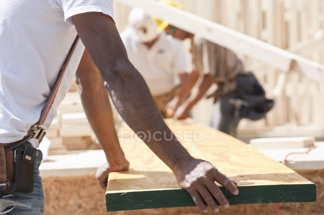 Carpinteiros segurando uma prancha em um canteiro de obras — Fotografia de Stock