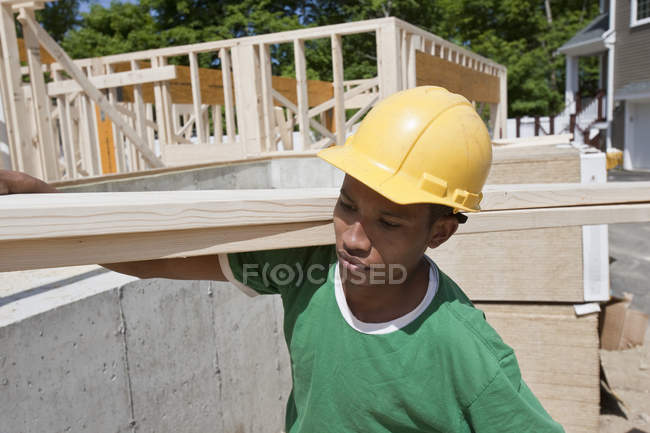 Carpintero llevando una plancha en un sitio de construcción - foto de stock